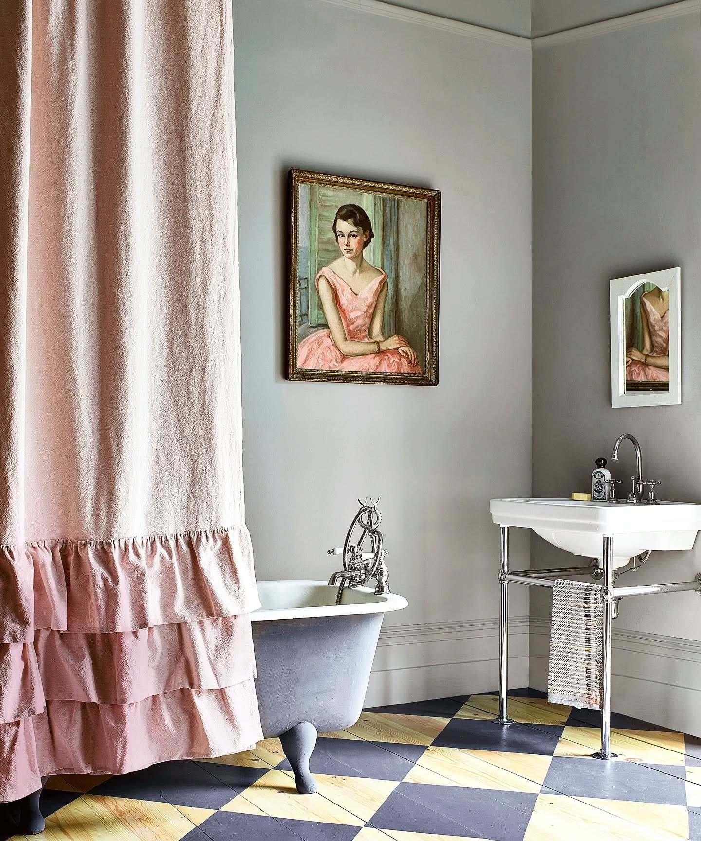 A solid dusty pink fabric shower curtain featuring several voluminous horizontal ruffles at the bottom, hanging over a classic clawfoot tub.