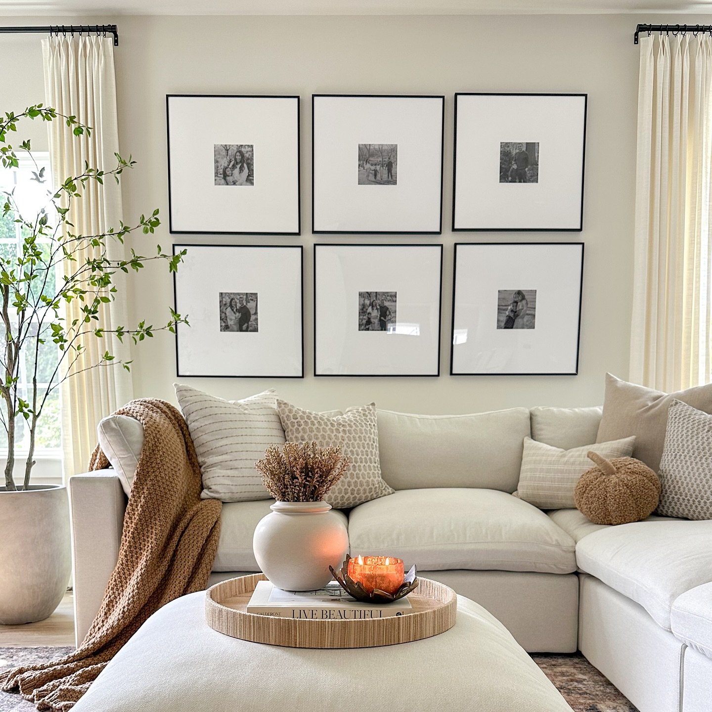A living room with a neutral color palette, a sectional sofa with a tan throw blanket, and a gallery wall of black and white photos.