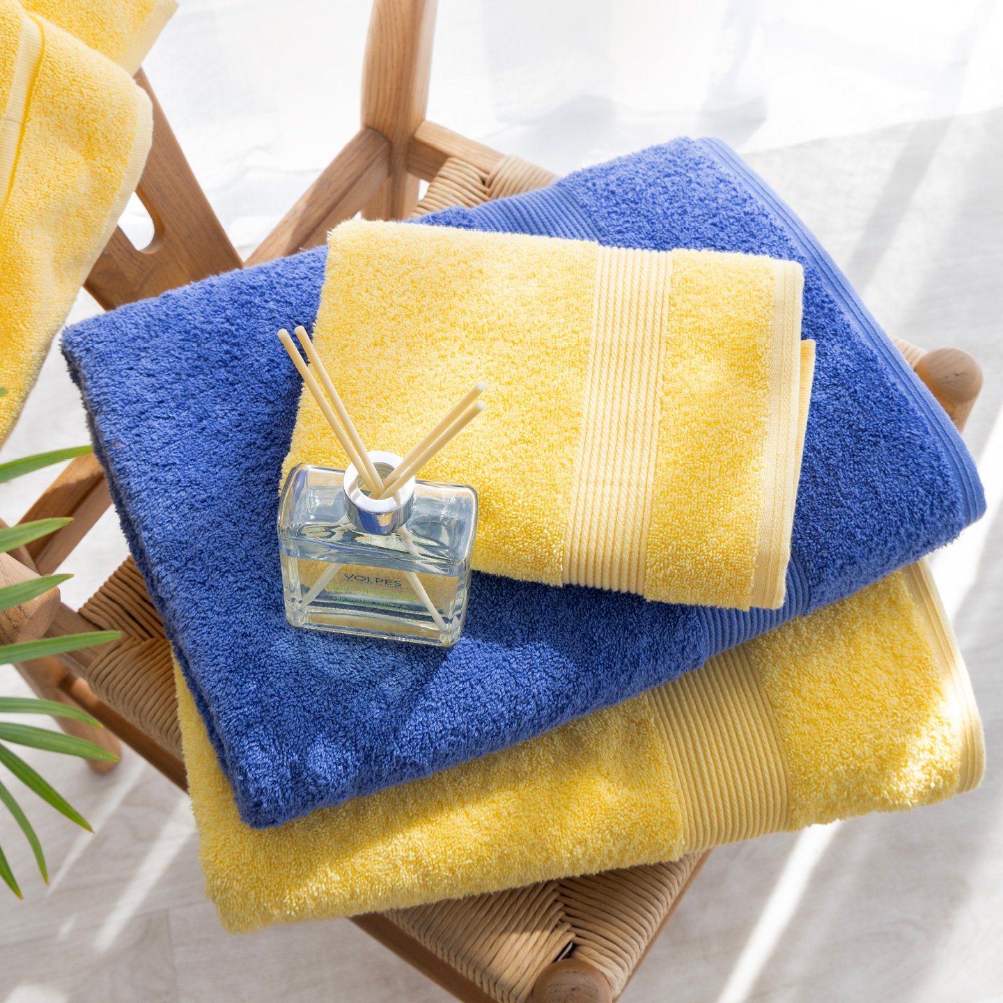 Stack of bright yellow and cobalt blue towels displayed on a cane chair with a small reed diffuser on top.