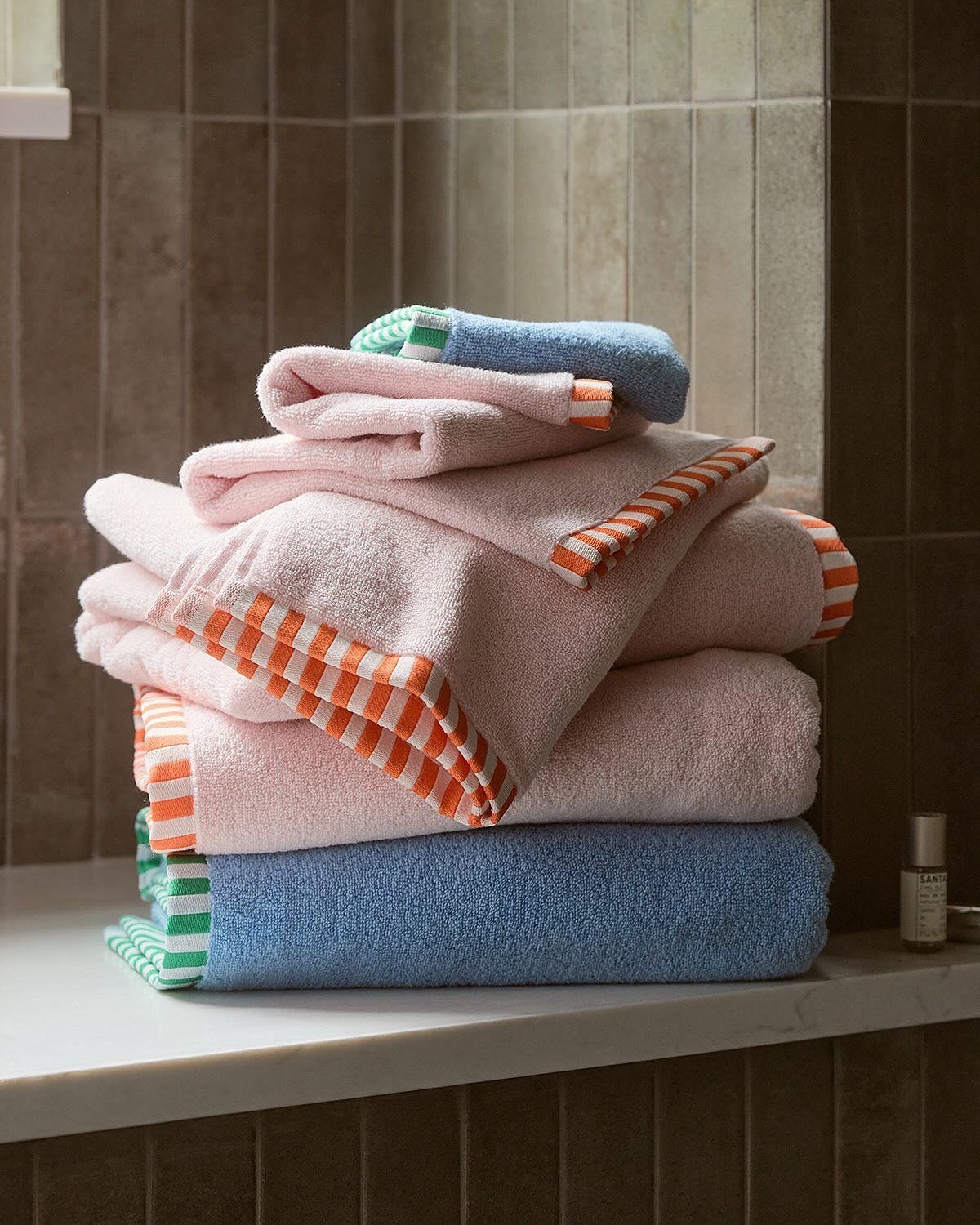 Stack of pink and blue bath towels with bold, contrasting borders: orange checkerboard and green stripe.