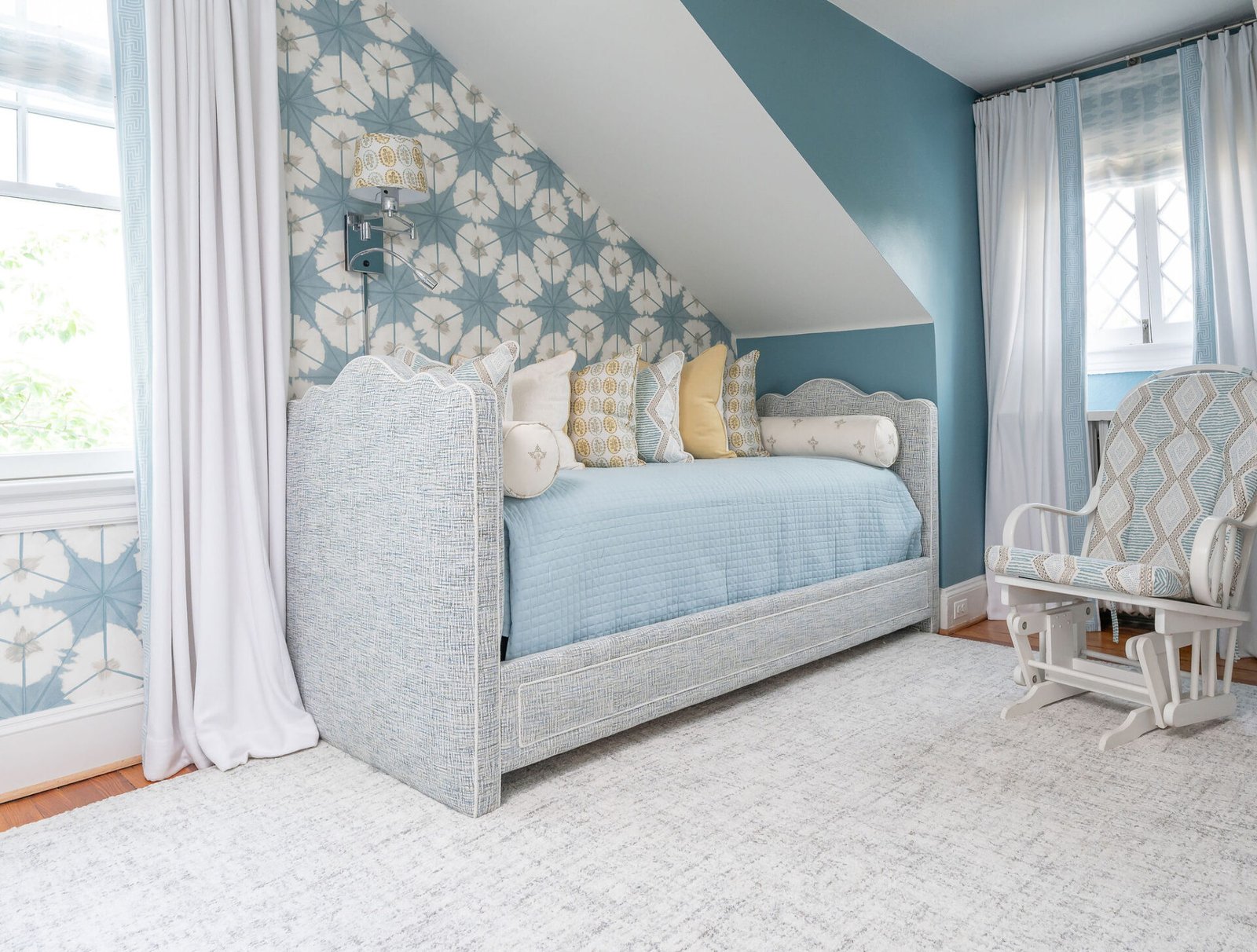 A colorful loft bedroom featuring a daybed with a patterned blue and white accent wall and a matching rocking chair.