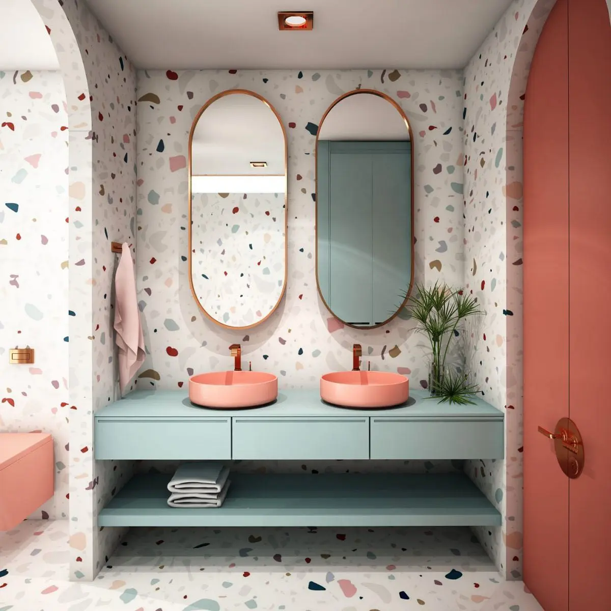 A colorful bathroom with a light blue floating double vanity featuring two pale pink vessel sinks and matching faucets. The walls and floors are covered in a vibrant terrazzo pattern with colorful flecks, and two tall oval mirrors with rose-gold frames hang above the sinks.