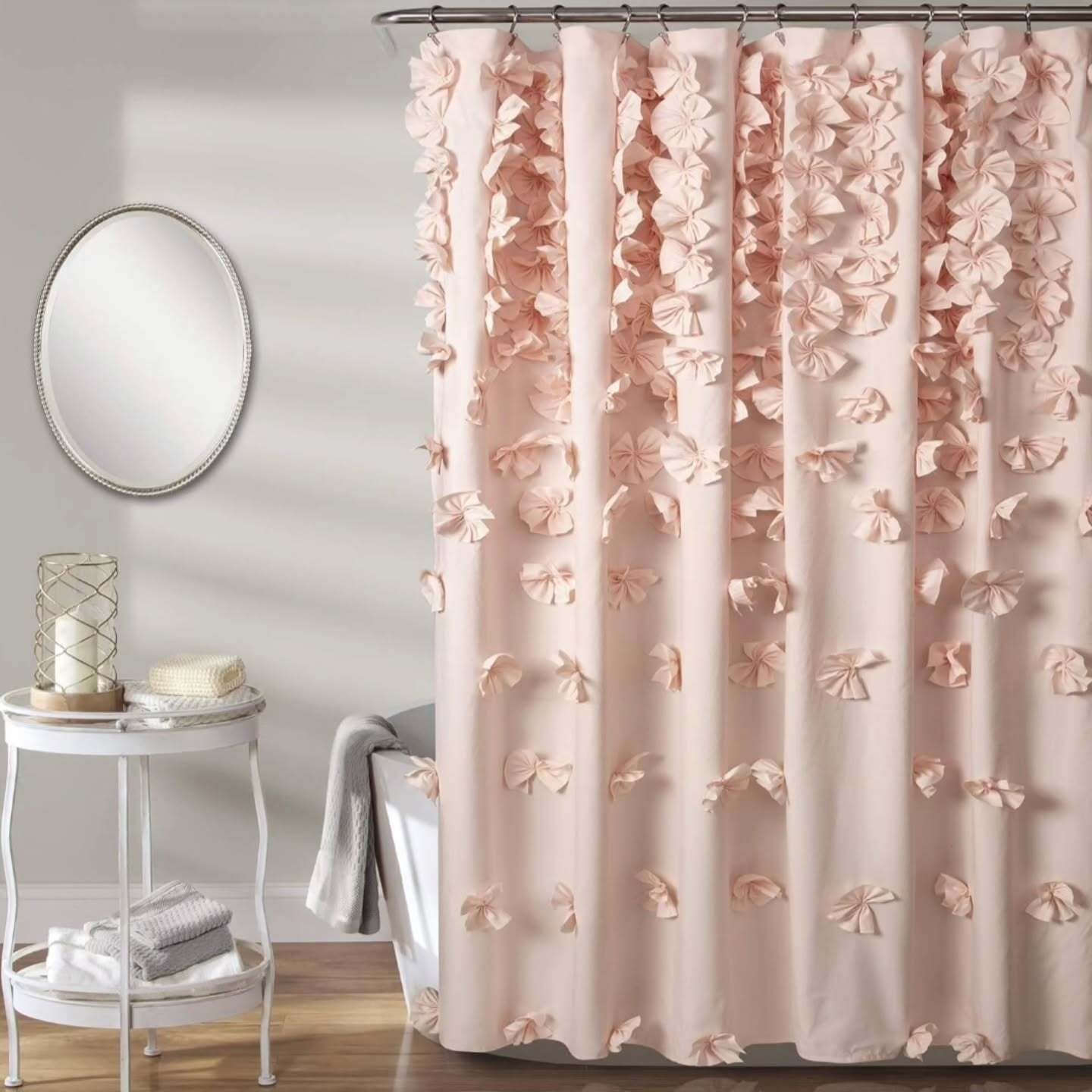 A solid blush pink shower curtain adorned with three-dimensional fabric bows that are densely clustered at the top and scatter down the length.