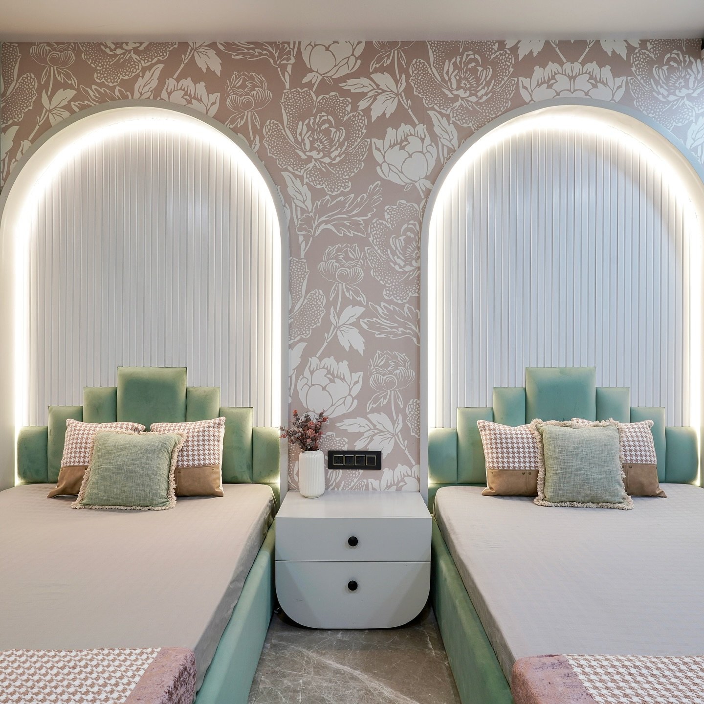 A luxurious twin bedroom with two beds, each placed inside a backlit arched alcove with fluted paneling and a mint green headboard.