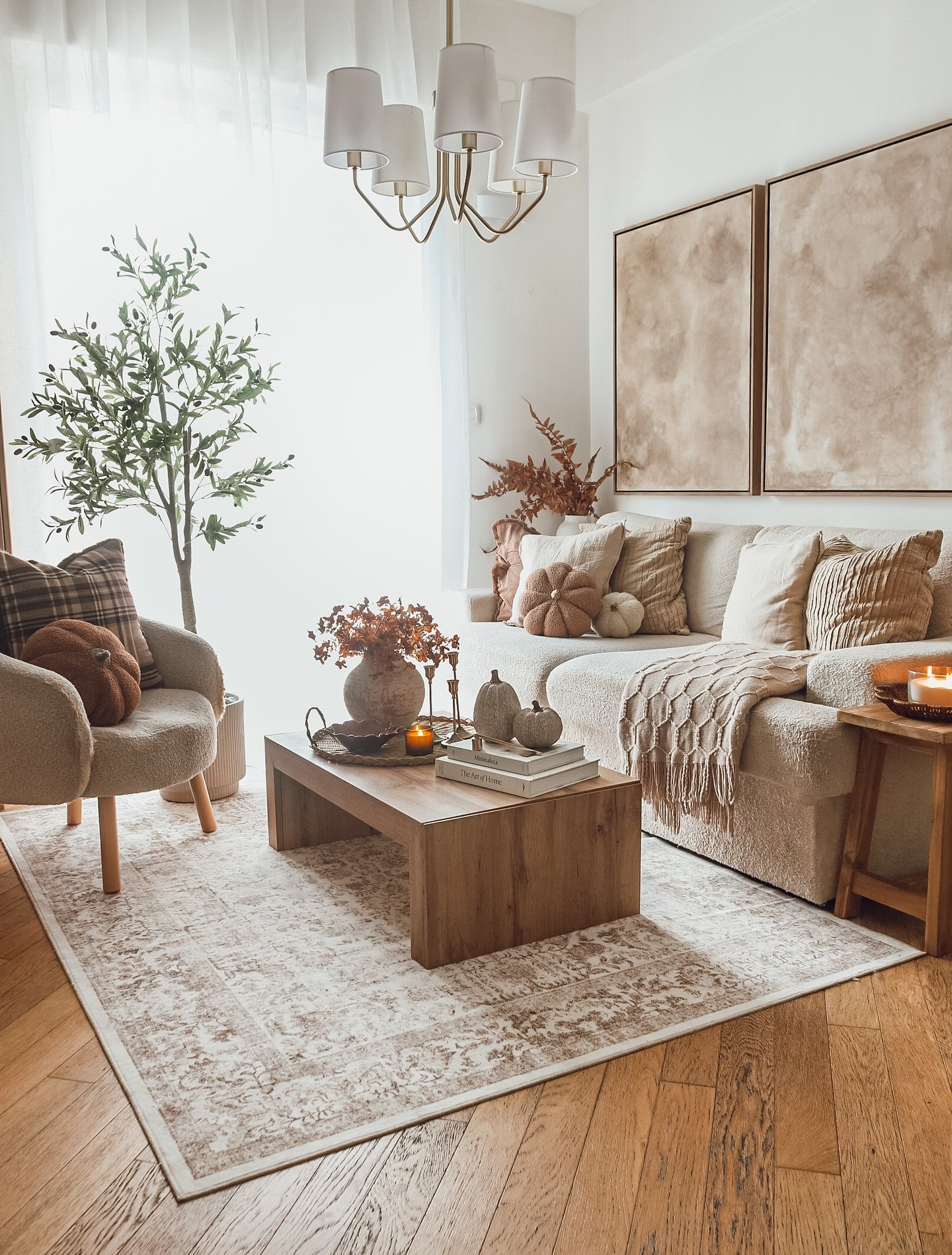 Living room with a beige boucle sofa, a rustic wood coffee table, and an armchair with a plaid pillow and a textured pumpkin.