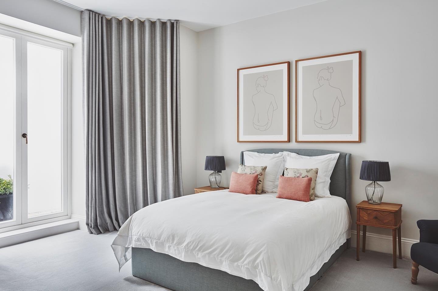 Gray wave-fold curtains beside a bed with white bedding and minimalist art prints.
