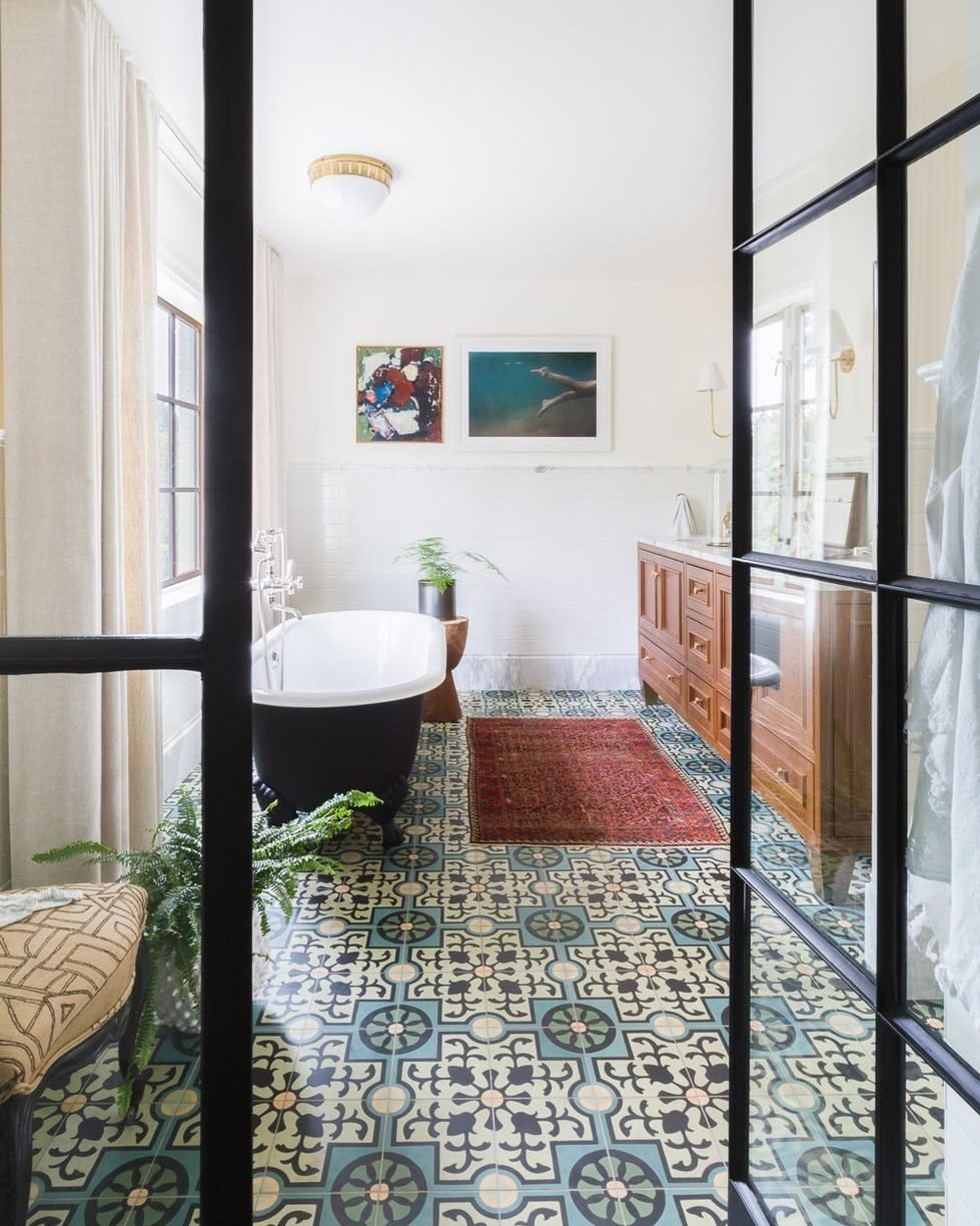 Close-up view of a bathroom floor featuring blue green and beige patterned cement tiles with a dark soaking tub and wooden vanity visible.