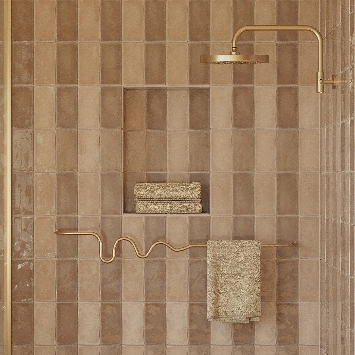 Unique wavy brass towel bar mounted on a warm beige tiled shower wall with stacked towels in a shower niche.