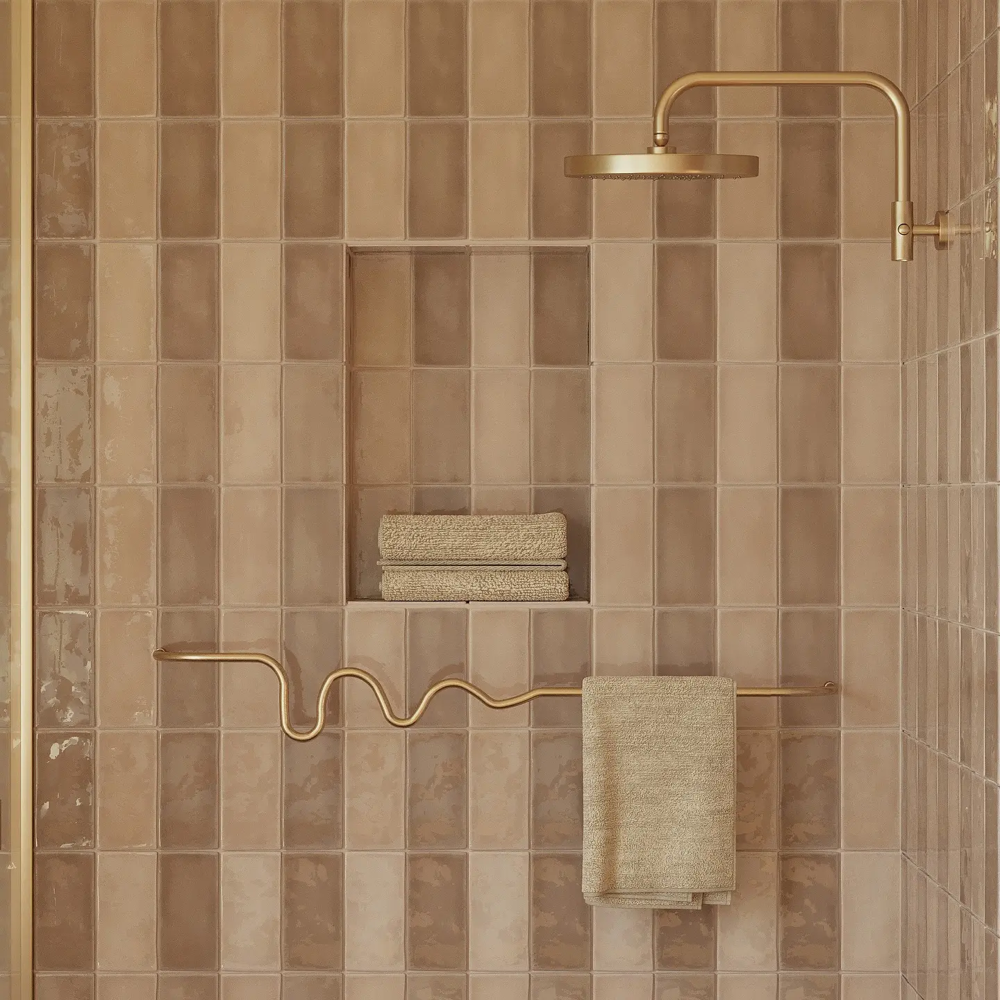 Unique wavy brass towel bar mounted on a warm beige tiled shower wall with stacked towels in a shower niche.
