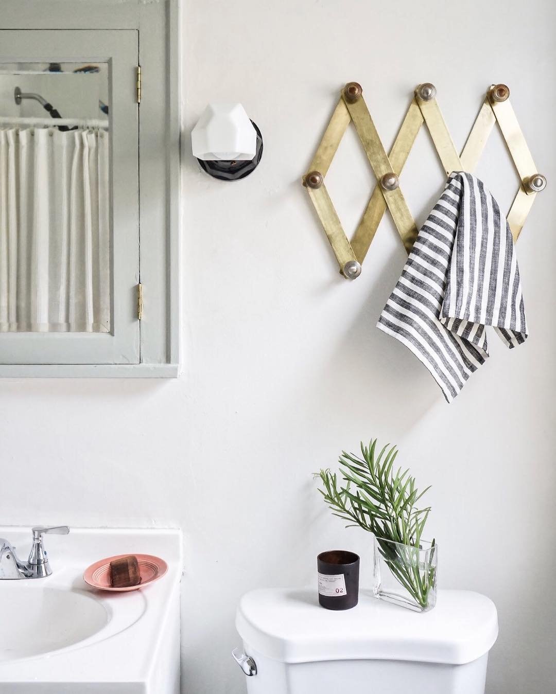 A brass expandable accordion peg rack holding a striped hand towel on a white bathroom wall.