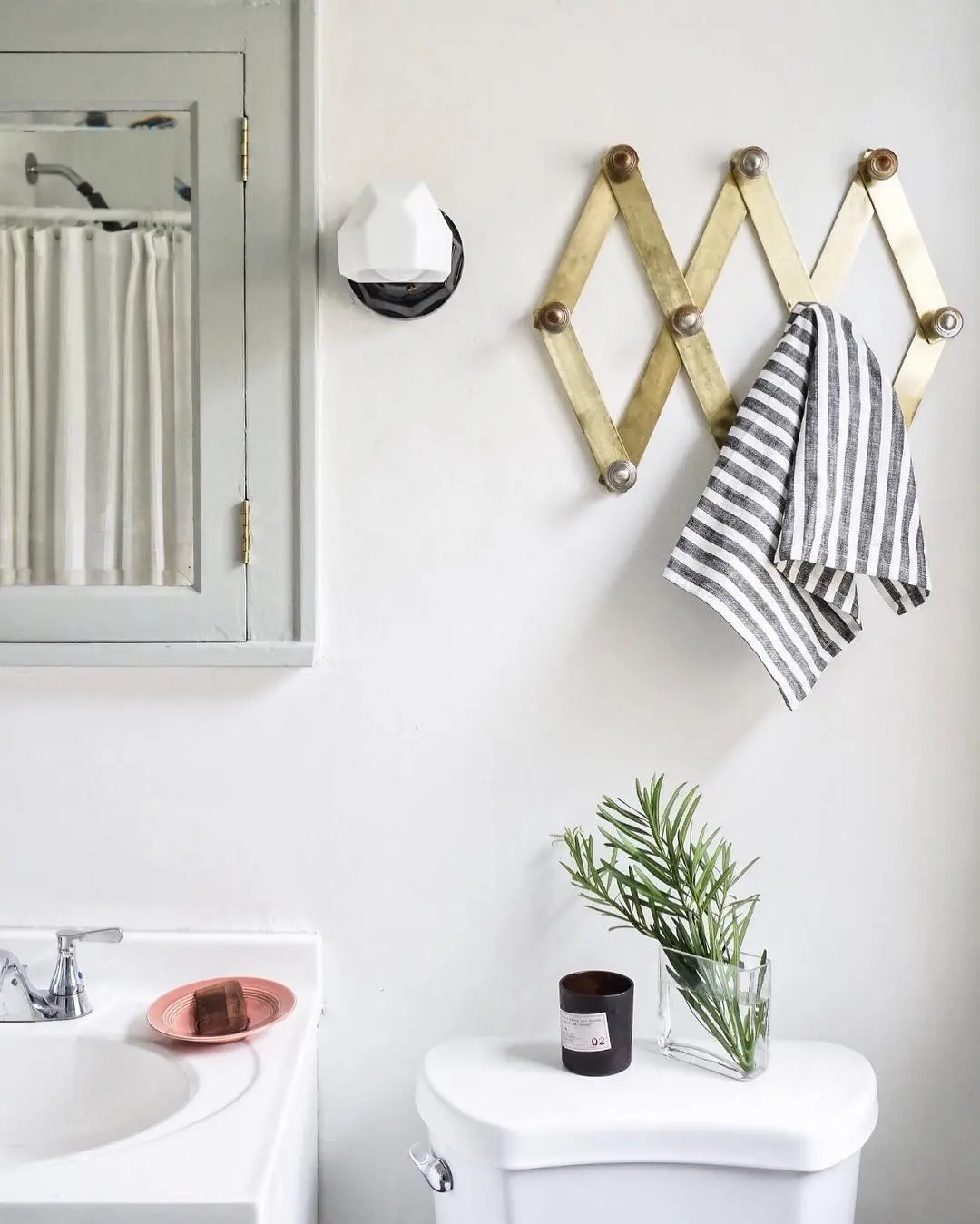 A brass expandable accordion peg rack holding a striped hand towel on a white bathroom wall.