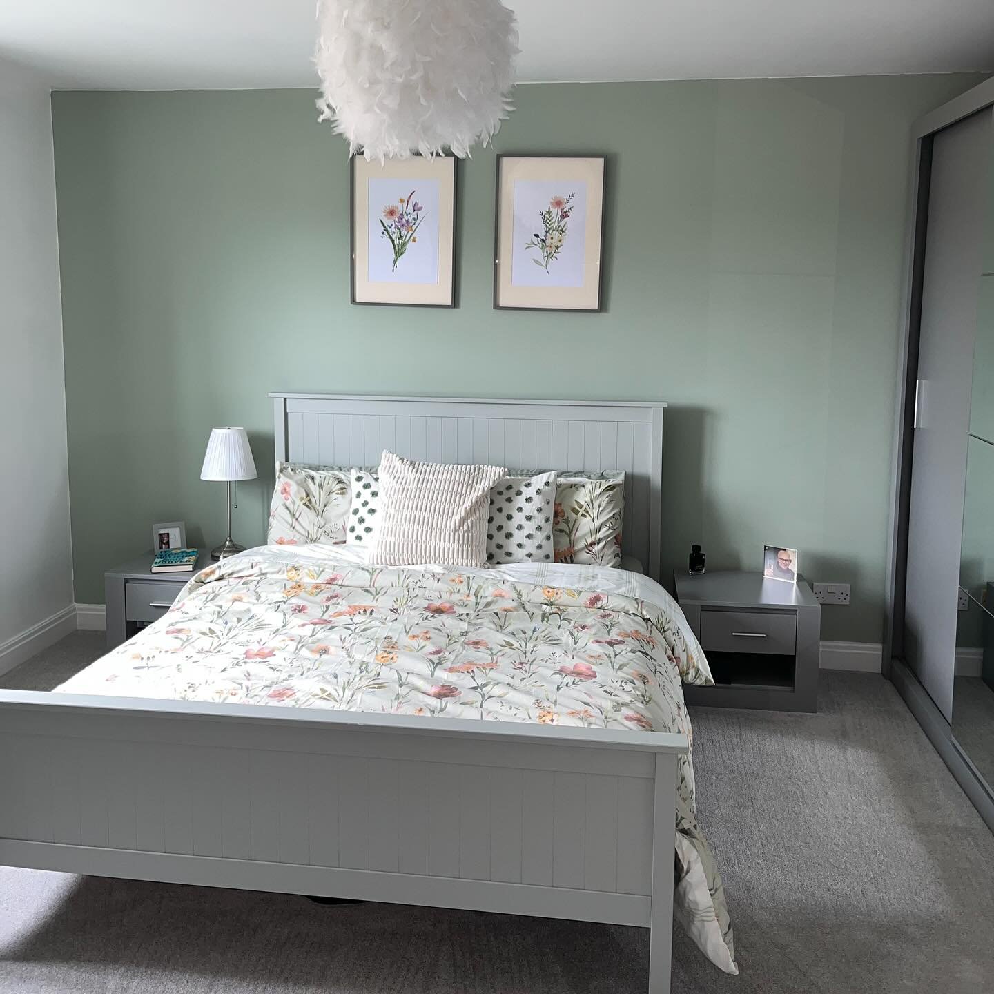 Bedroom with a sage green accent wall, light grey wooden furniture, and floral duvet cover.
