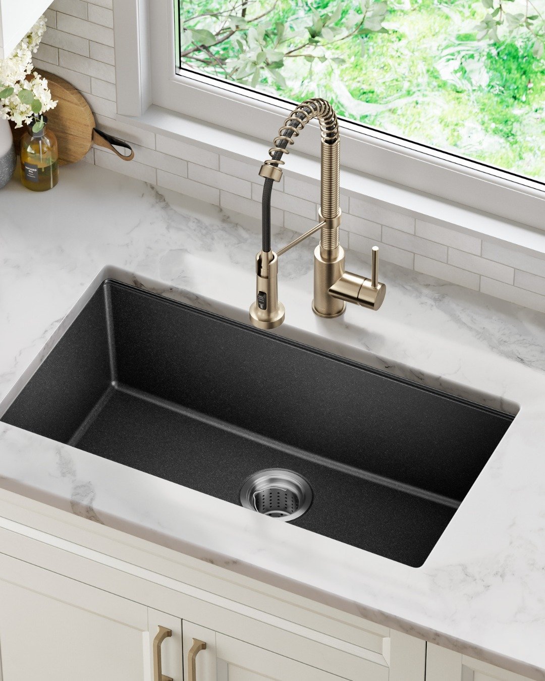 Large single-bowl black granite composite sink with a brushed gold pull-down faucet and white marble countertop.