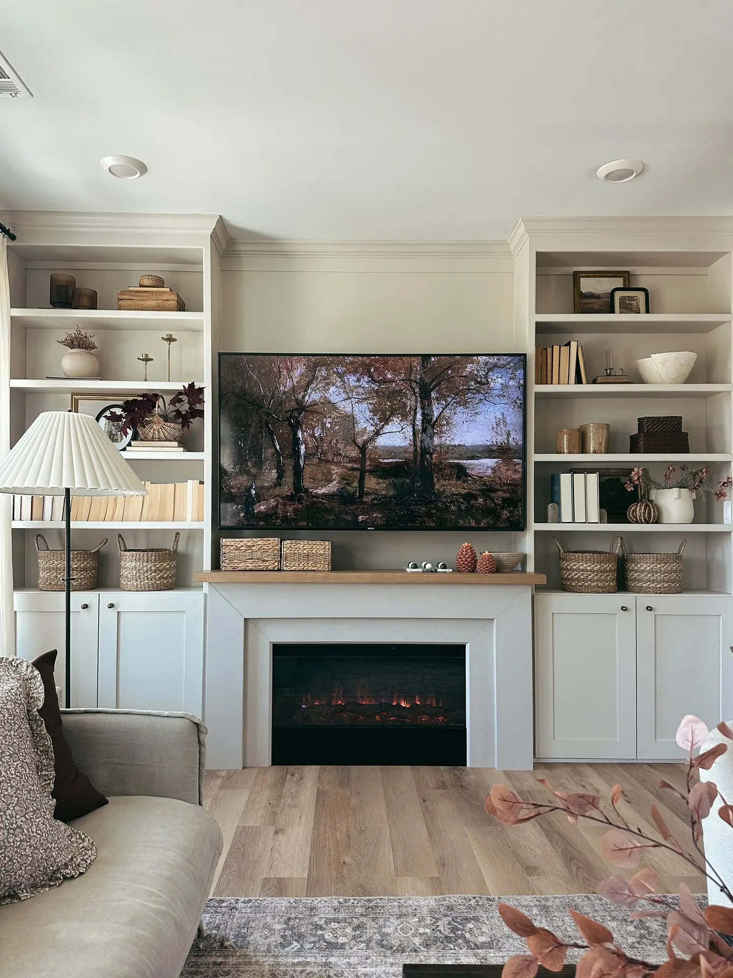 Traditional living room featuring a wall of light grey custom built-in bookshelves with a central electric fireplace and a TV mounted above a wooden mantel shelf.