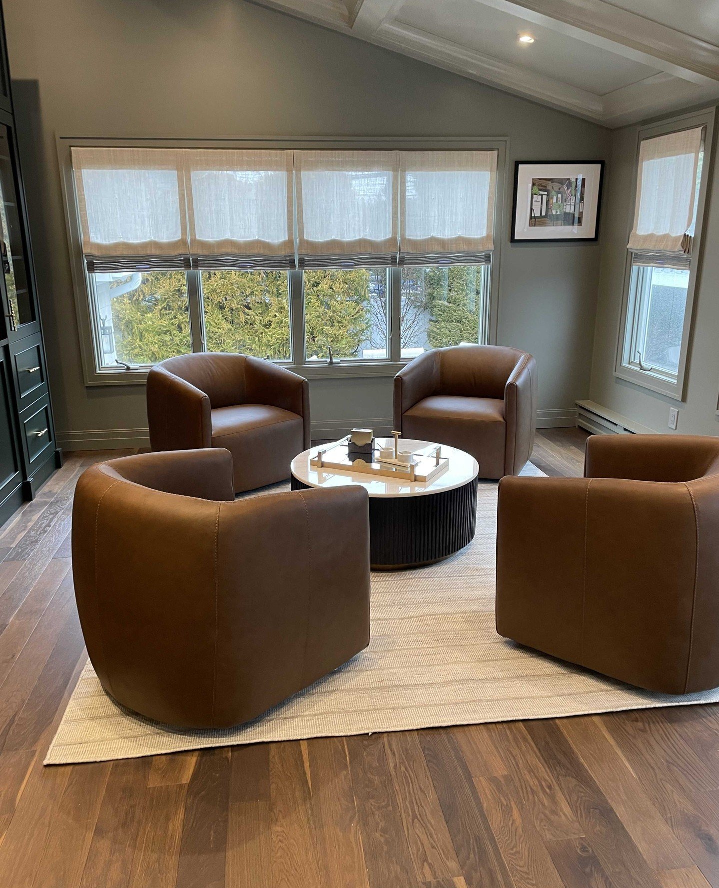 Four brown leather swivel club chairs facing a round coffee table on a neutral rug.