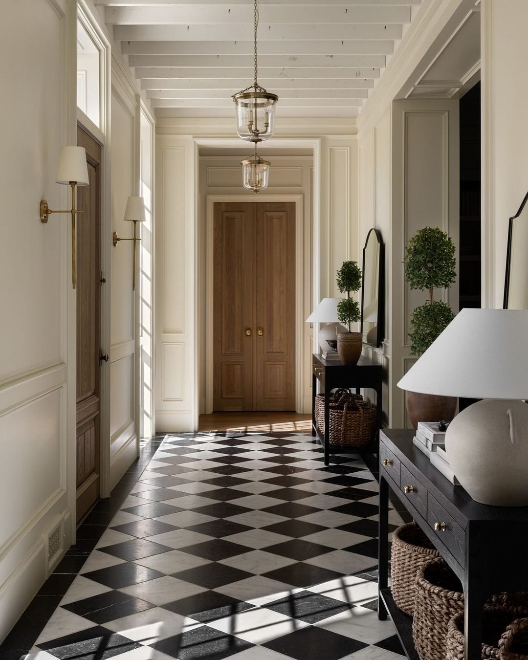 Traditional entry hall with black and white checkerboard floor, brass wall sconces, and overhead glass lantern pendants.