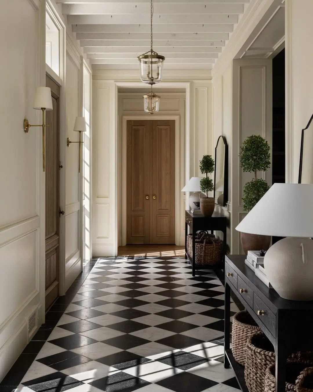 Traditional entry hall with black and white checkerboard floor, brass wall sconces, and overhead glass lantern pendants.