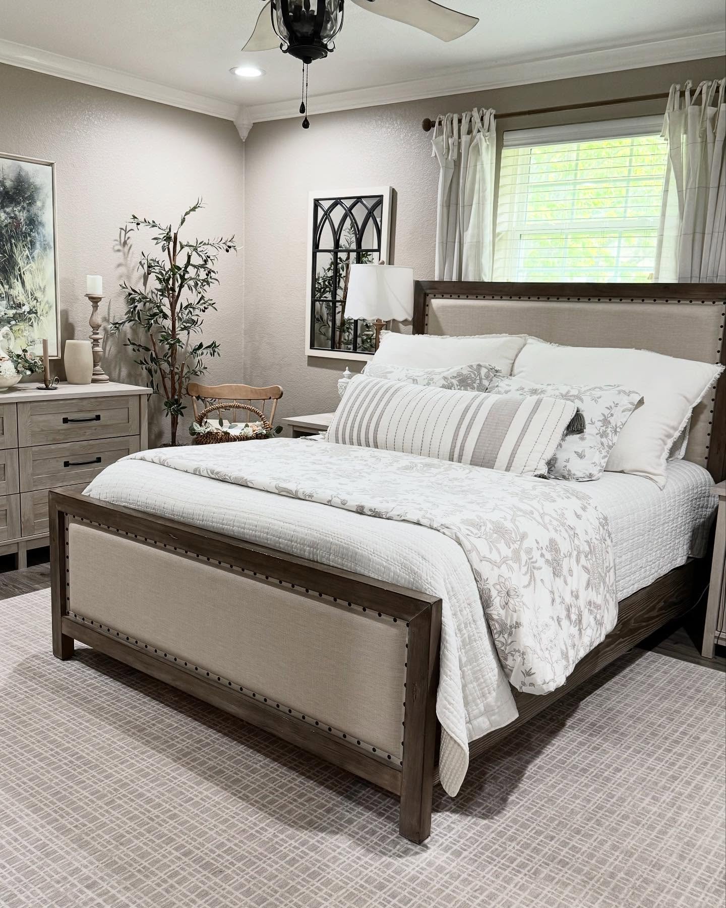 Cozy farmhouse bedroom with wood and linen bed. Neutral color palette of white, gray, and beige.