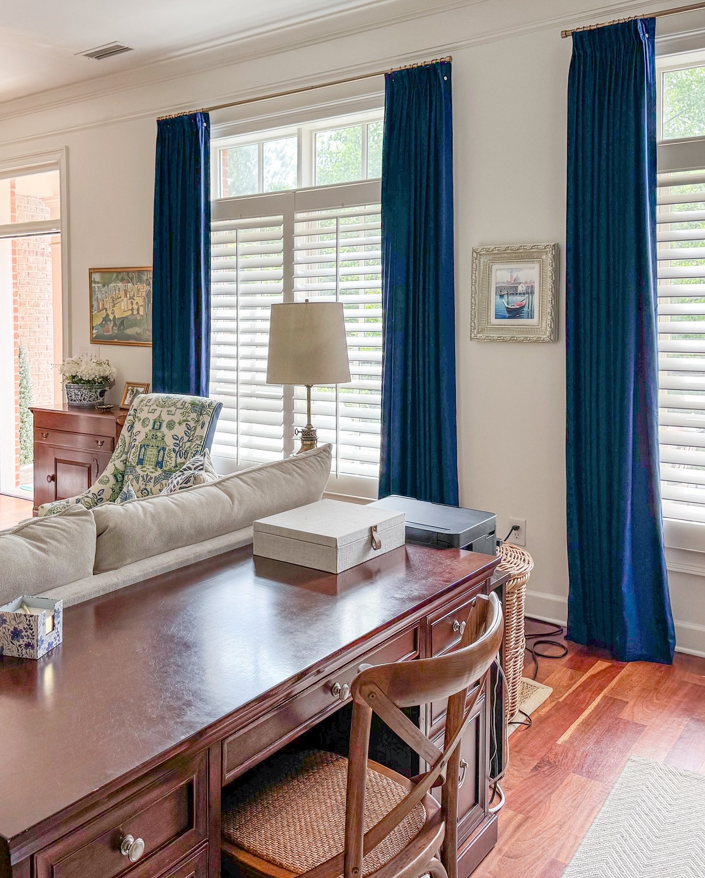 Floor-length navy blue velvet curtains flanking a white window with interior plantation shutters in a traditional living room.