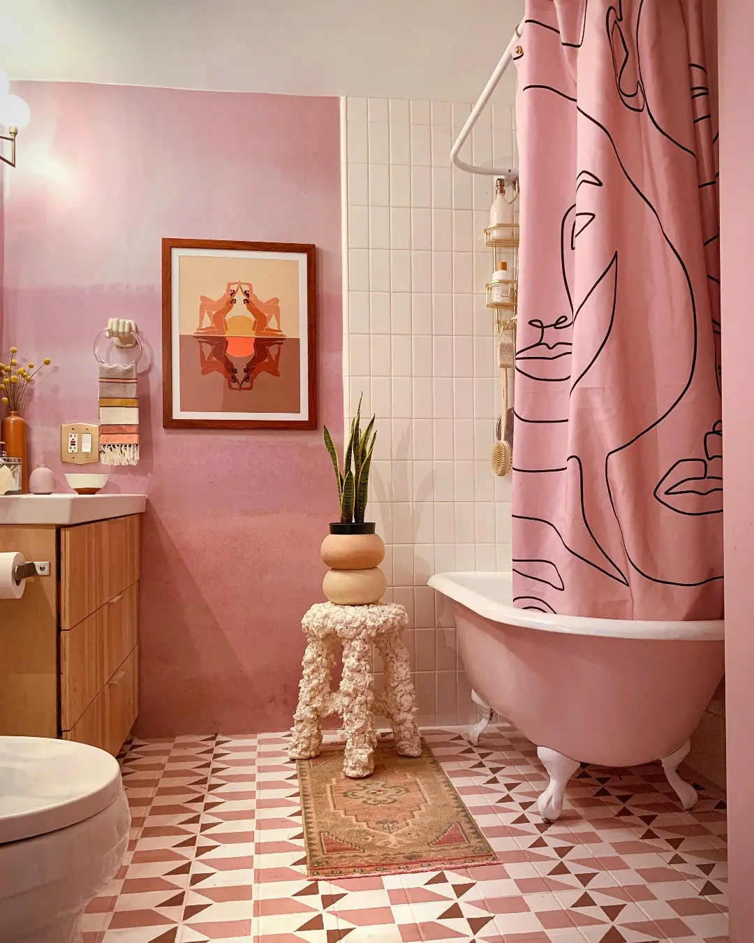 A colorful bathroom with pink walls and tile, featuring framed abstract art and a pink clawfoot tub.