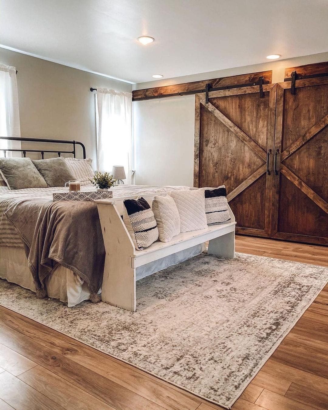 Cozy farmhouse bedroom with warm wood floors, neutral bedding, and a striking pair of rustic sliding barn doors used for a closet.