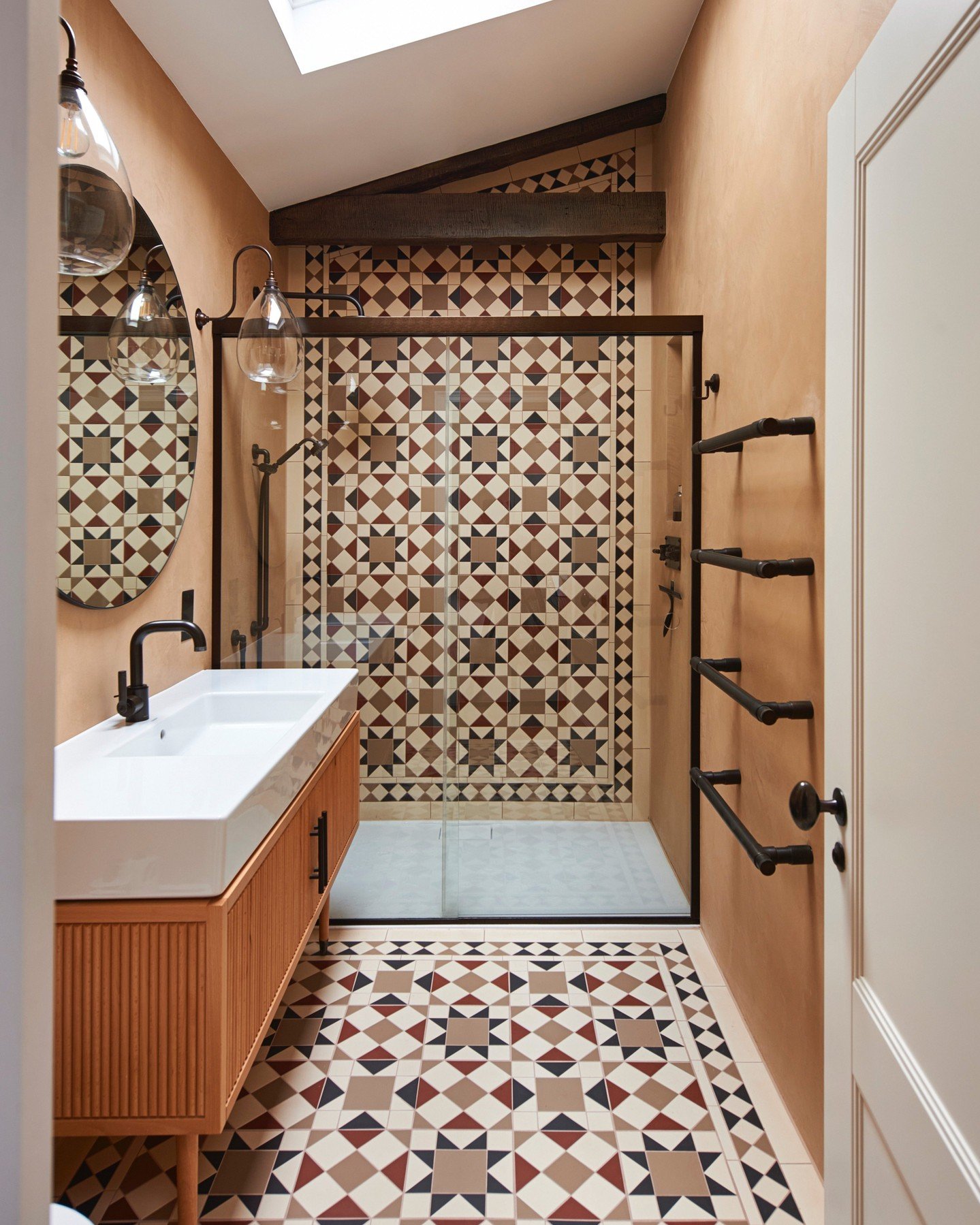 A small, warm-toned bathroom featuring a mid-century vanity and a floor covered in geometric patterned cement tiles with brown, cream, terracotta, and dark red colors.