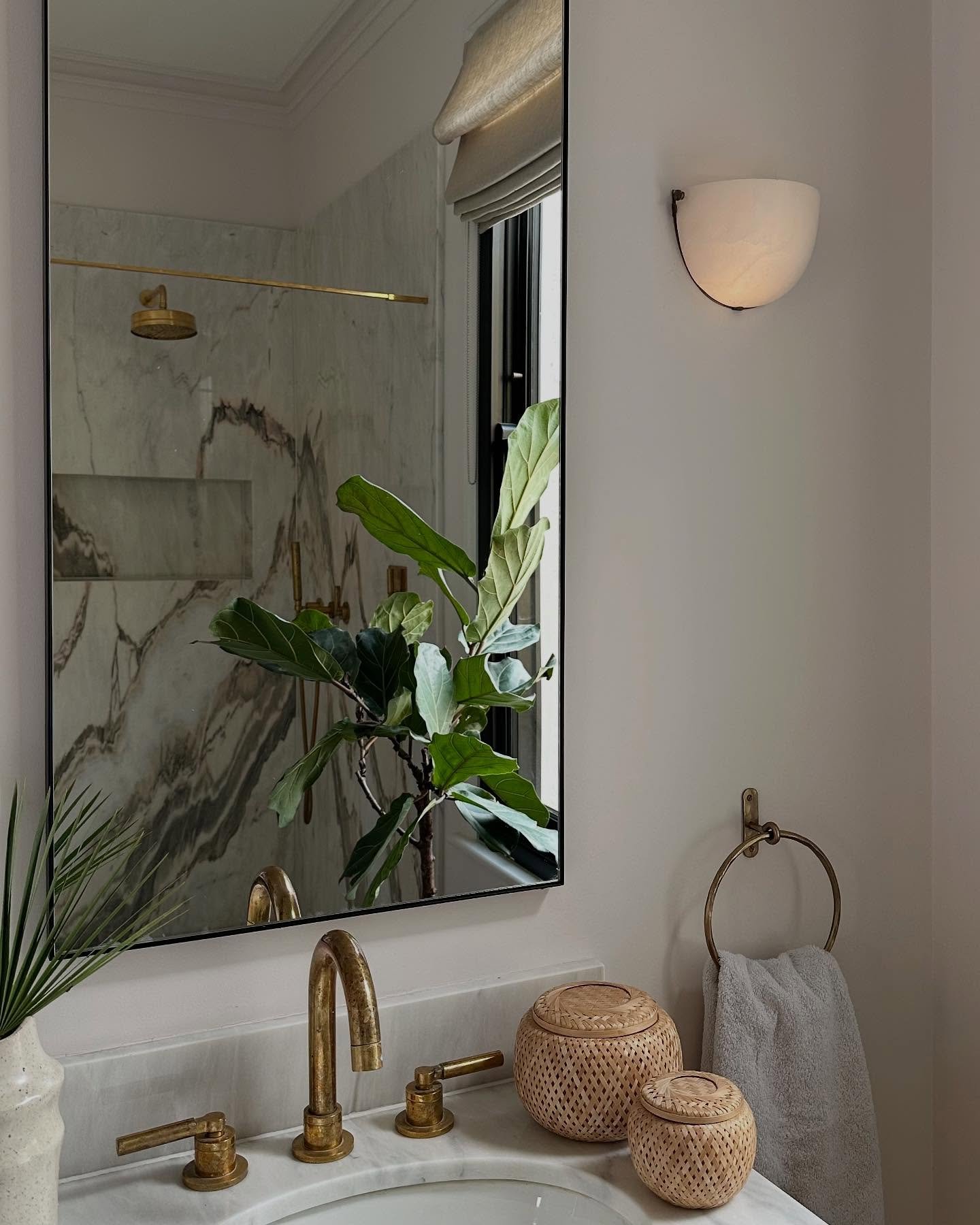 An aged brass hand towel ring holding a light gray towel next to a white marble countertop and brass faucet.