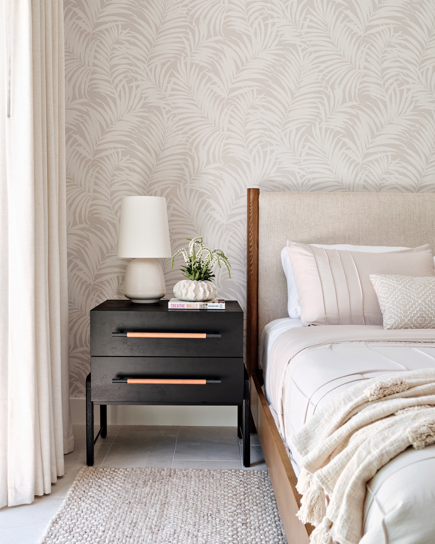 Dark wood nightstand with two drawers and warm brown leather pull handles, set against a palm-leaf patterned wallpaper.