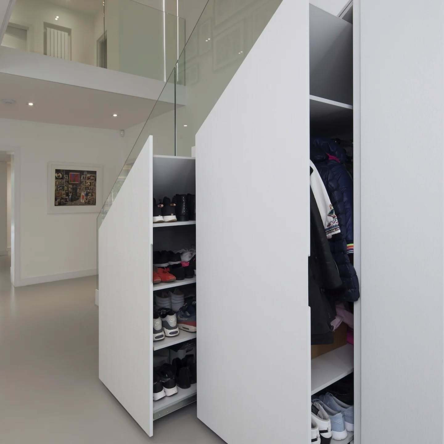 Large, white custom pull-out drawers under a staircase, one drawer revealing stacked shoe shelves.
