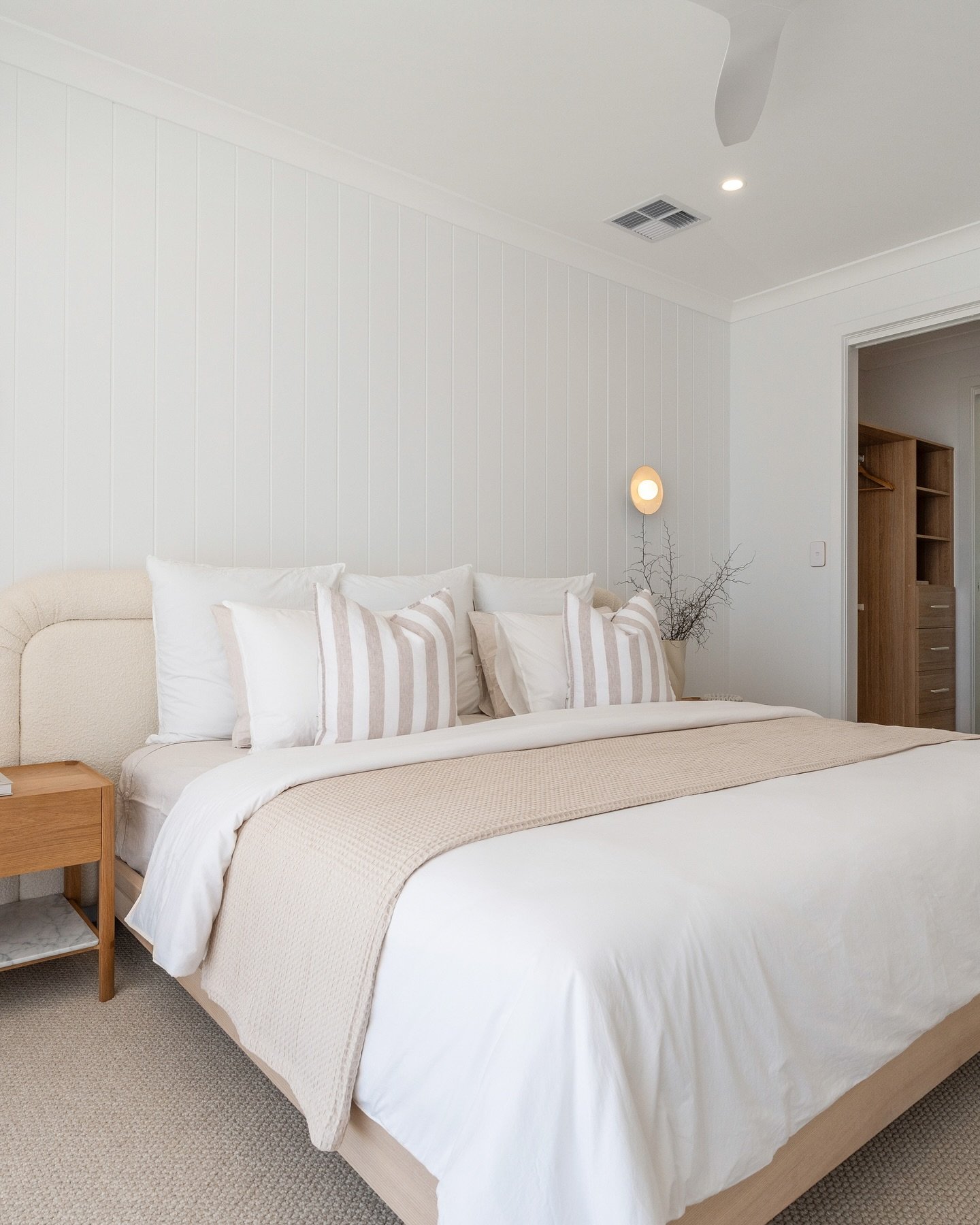 Bright bedroom with a shiplap accent wall, a curved upholstered headboard, crisp white bedding, and beige striped throw pillows.