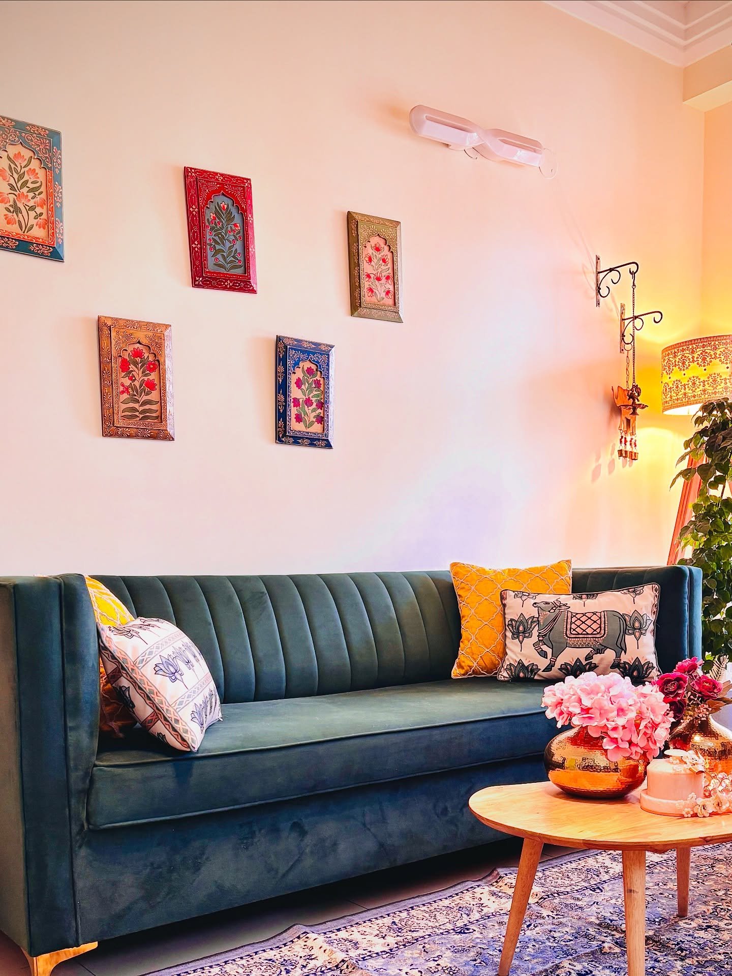 Asymmetrical cluster of five small, ornate framed Indian miniature floral paintings hung above a blue velvet channel-tufted sofa.