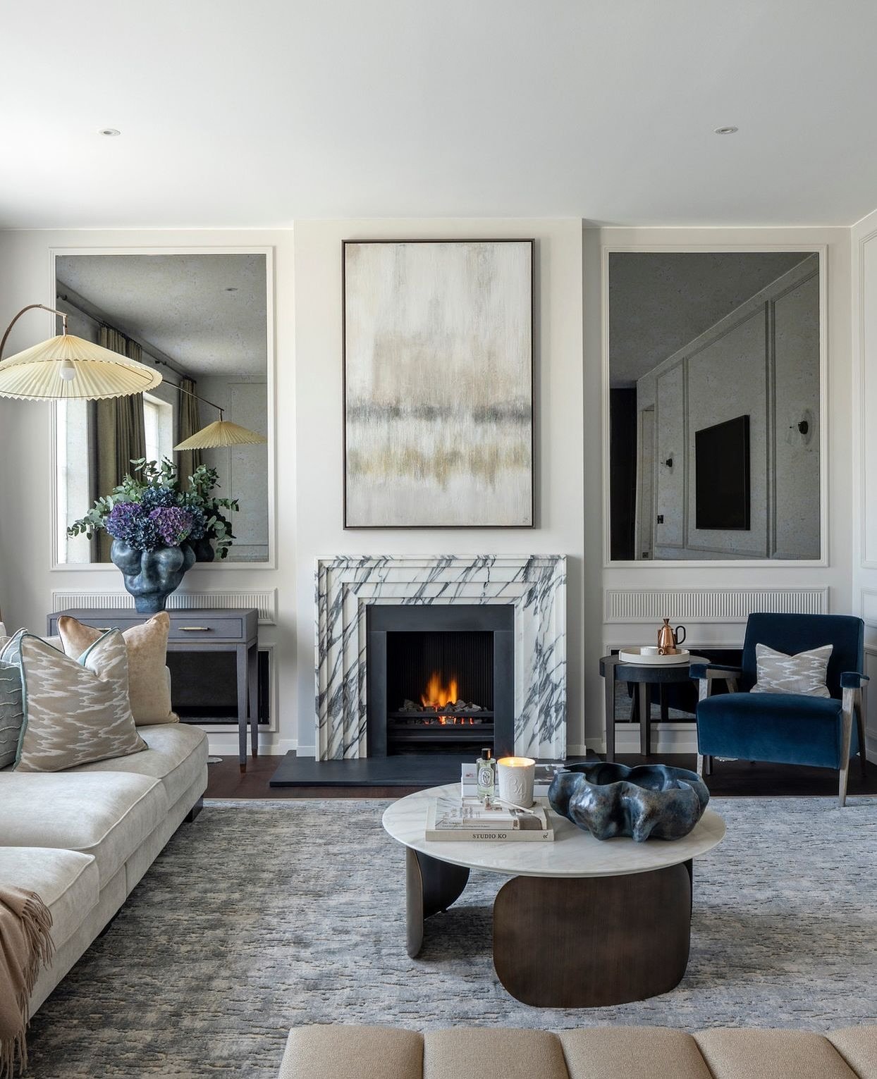 Elegant living room with a white and gray veined marble fireplace surround, flanked by two large, antique-style wall mirrors.