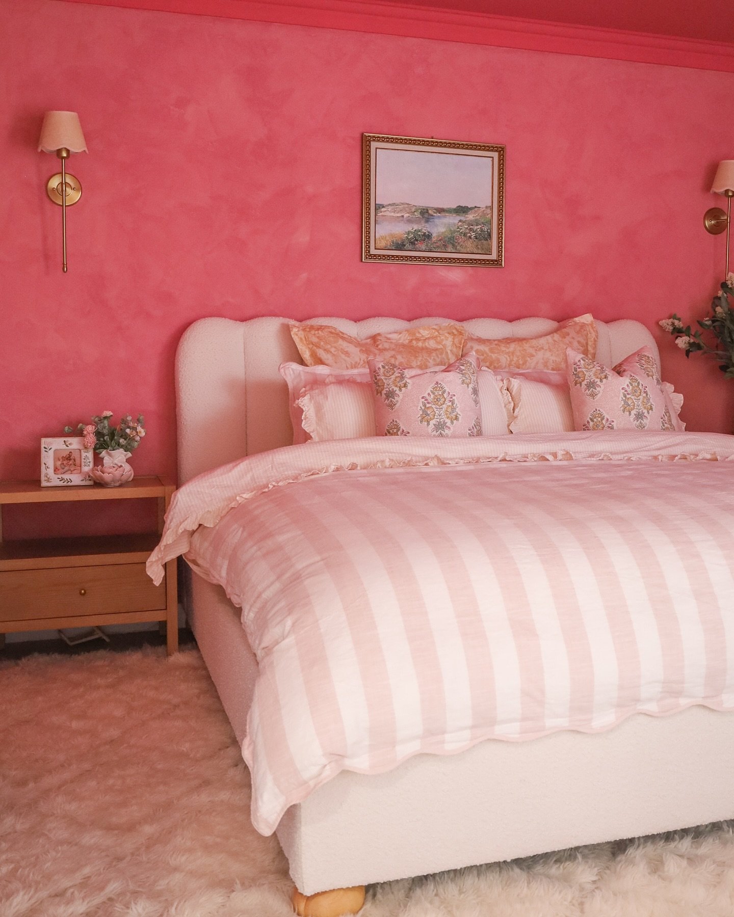 Bedroom with deep textured pink walls, a light pink and white gingham duvet, and a white curved bouclé headboard.