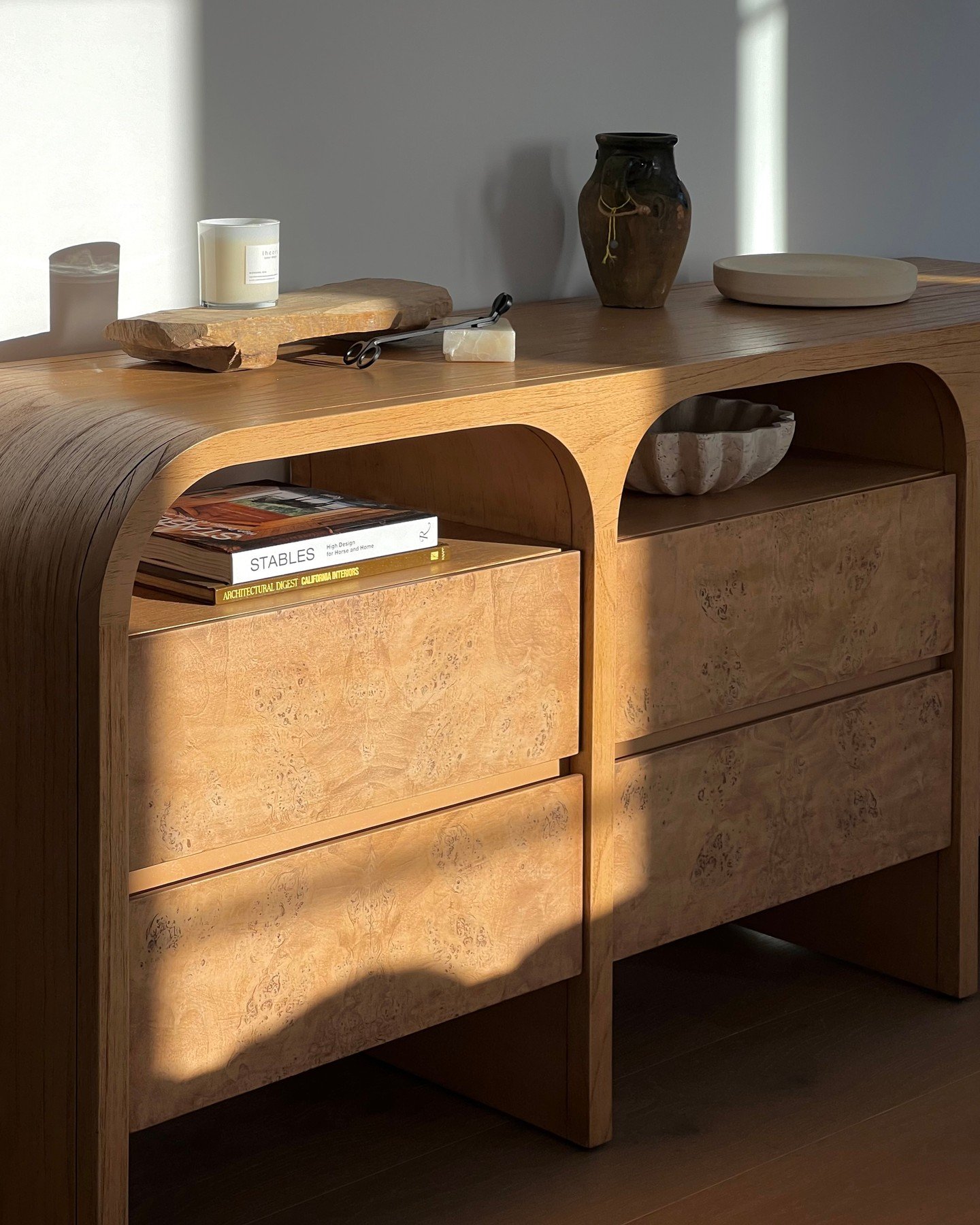 Close-up of a modern wooden dresser with a curved silhouette, featuring two large drawers with decorative burl wood fronts and an open shelf above each drawer.