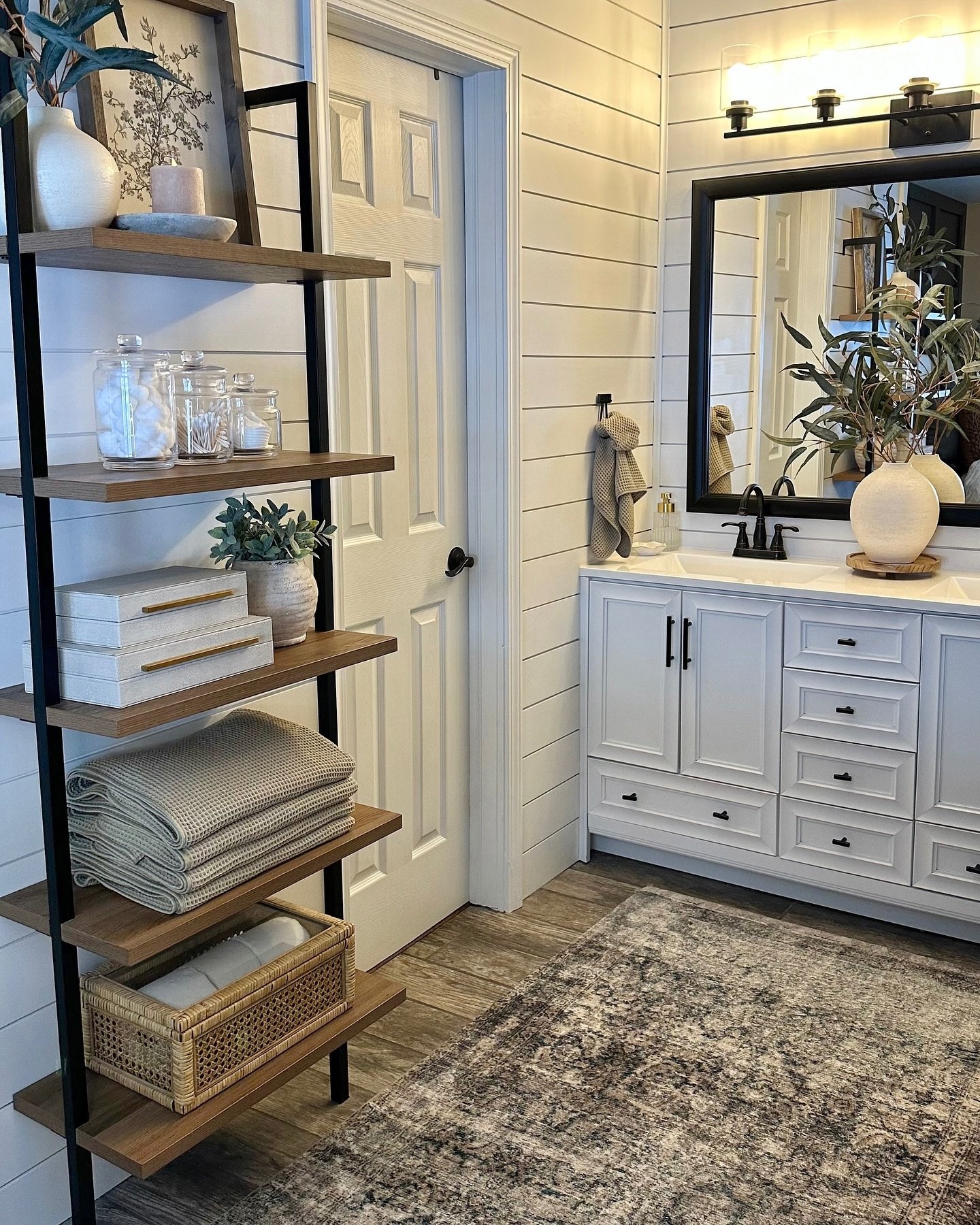 A tall, five-tier leaning ladder shelf with dark metal supports and warm wood shelves, styled with boxes, folded textiles, and clear jars.
