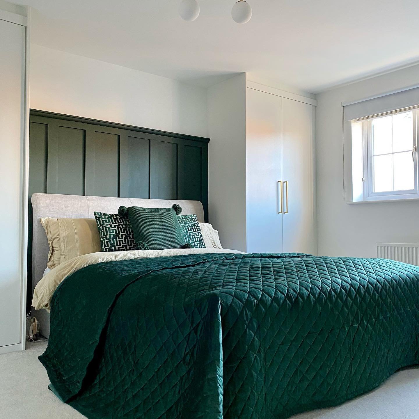 Bedroom featuring a dark green wood panelled structure built into the alcove behind the bed, with a quilted emerald bedspread.