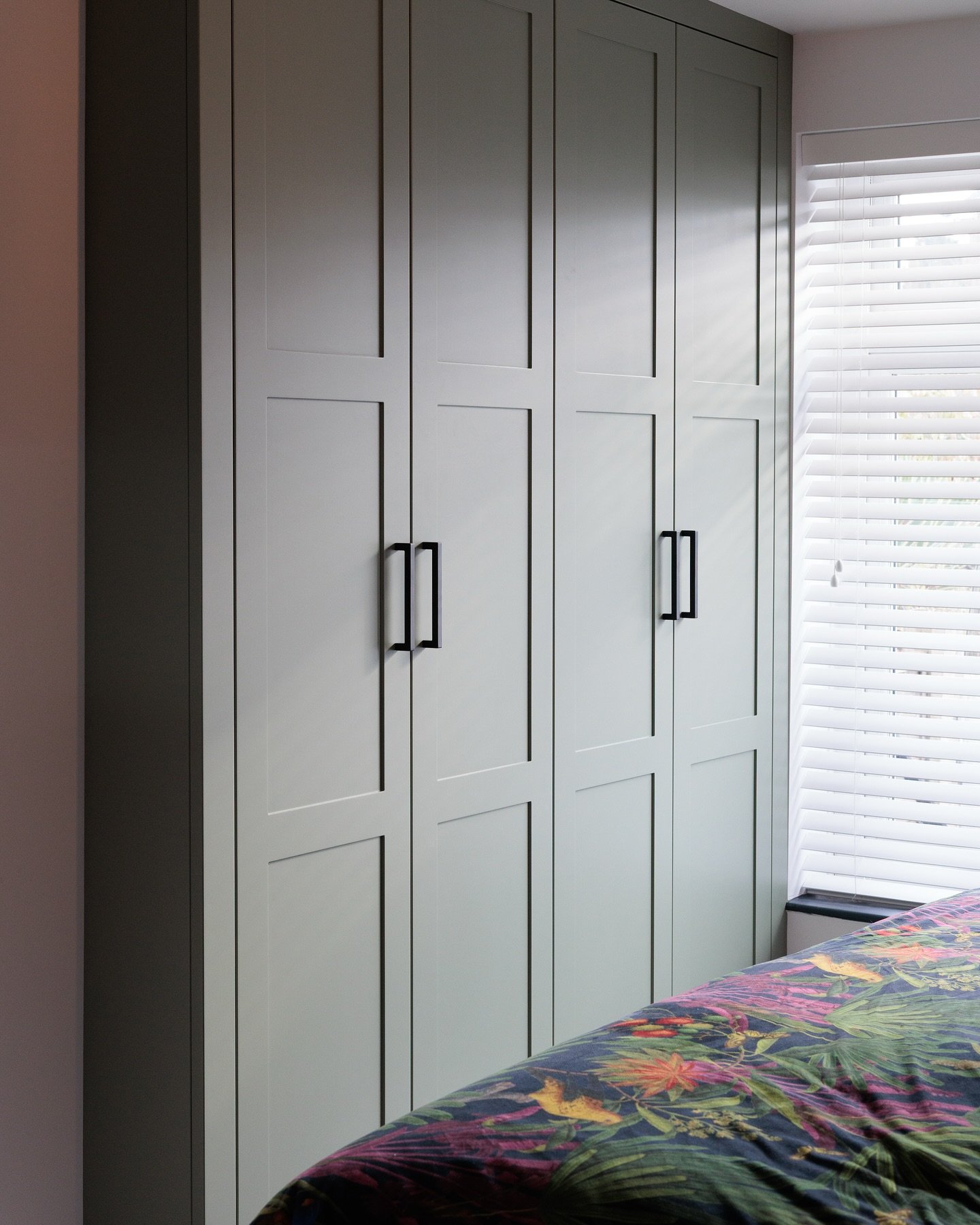 Built-in wardrobe with a muted sage green finish, featuring two-panel shaker-style doors and minimalist matte black bar handles.