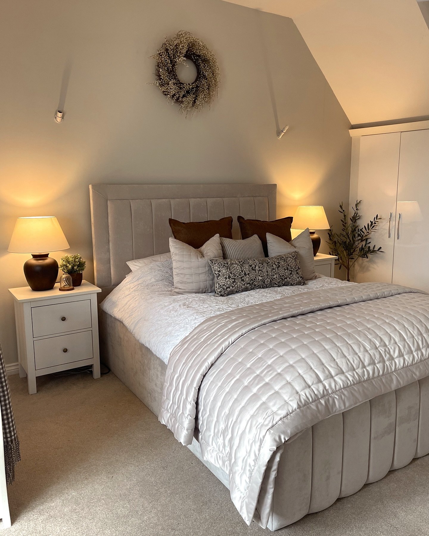 Cozy bedroom with a channel-tufted velvet bed in a soft beige, layered with quilted bedding, and dark accents.