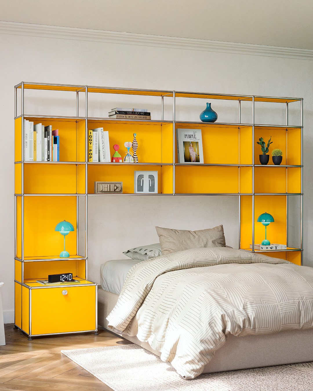 A modular shelving unit with bright yellow paneling and chrome framing built around the head of a bed, featuring open storage for books and small items, with the bottom units acting as integrated nightstands.