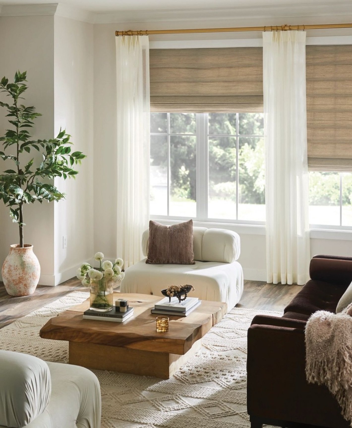 Layered window treatment featuring light sheer curtains and natural woven wood Roman shades in a bright living room.