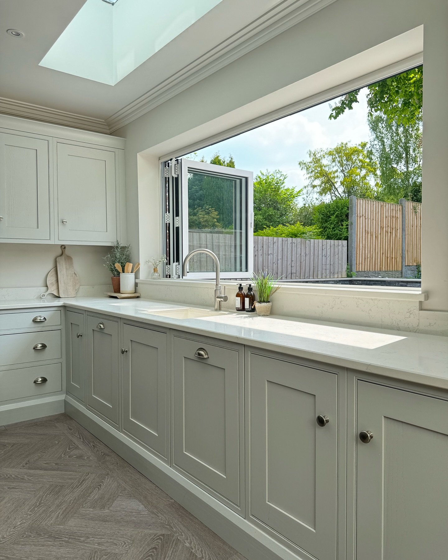 Kitchen with light gray shaker cabinets and white counters. A large, horizontal bi-fold window opens completely to the backyard, creating a seamless indoor-outdoor connection.