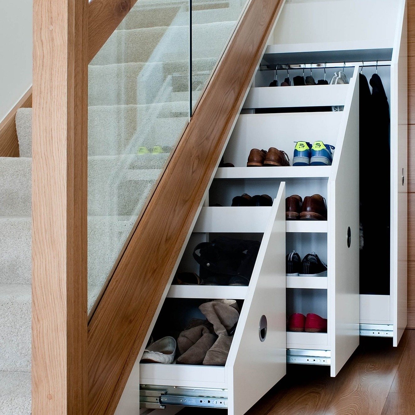 White, stepped, sliding drawers and a tall closet pulling out from under a modern glass staircase.