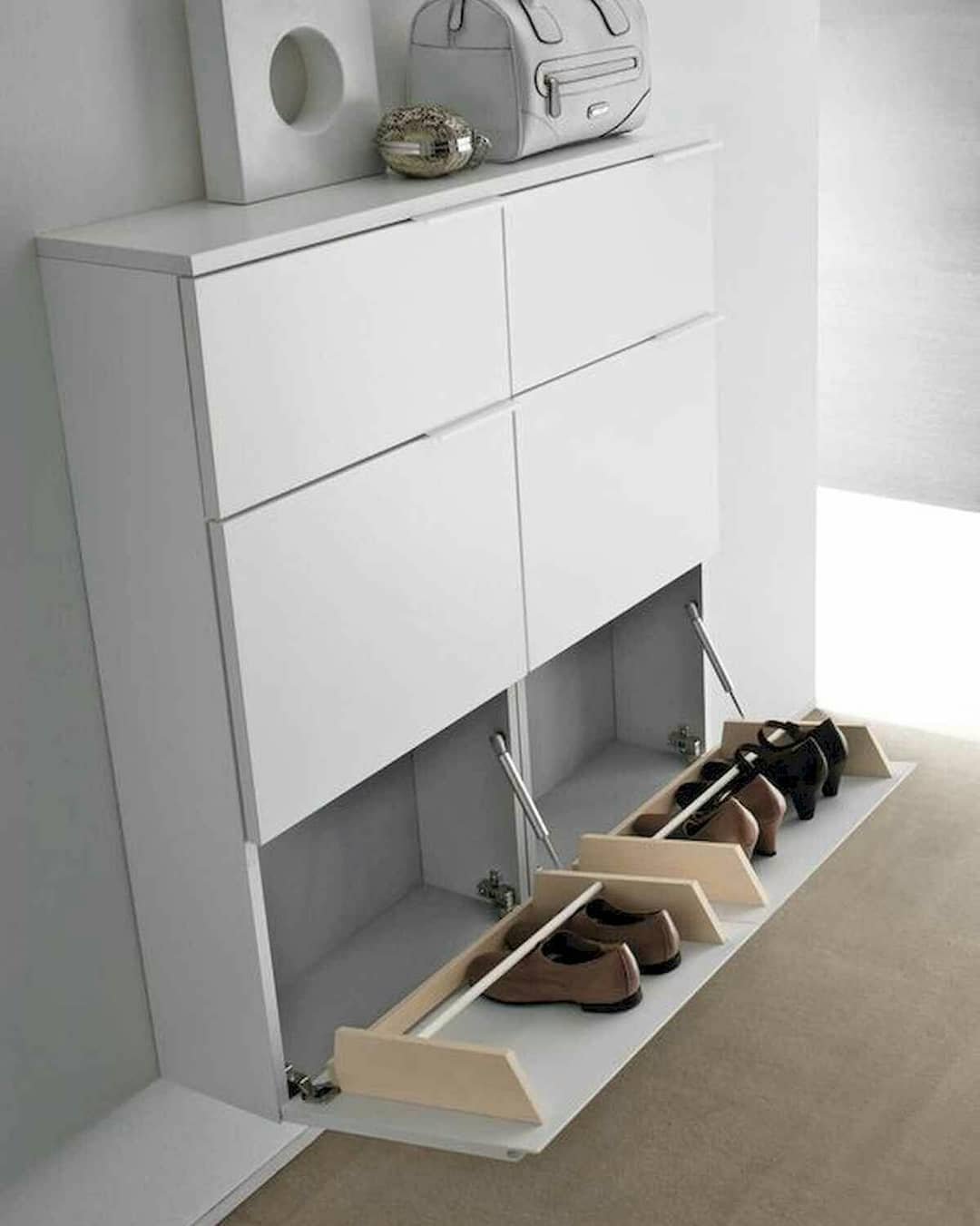 Sleek white shoe cabinet with two lower tilt-out drawers angled open to reveal shoes stored vertically.