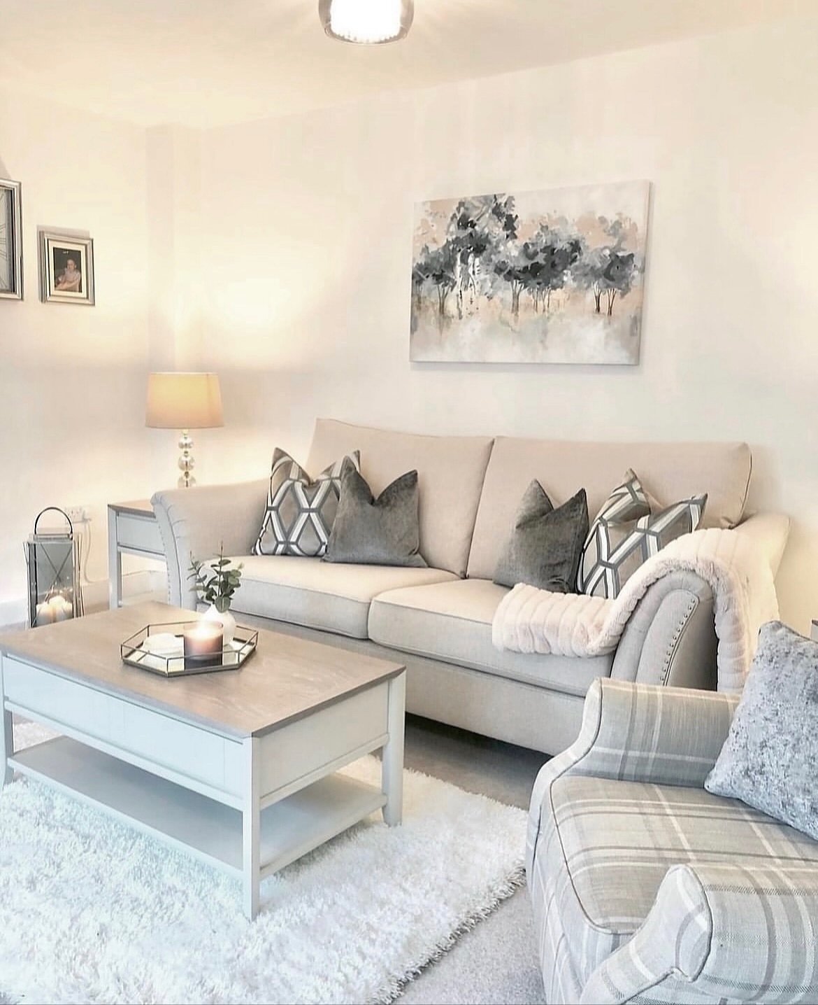 Horizontal abstract painting of a muted grey and pink misty woodland, hung unframed above a beige sofa in a cozy, neutral living room.