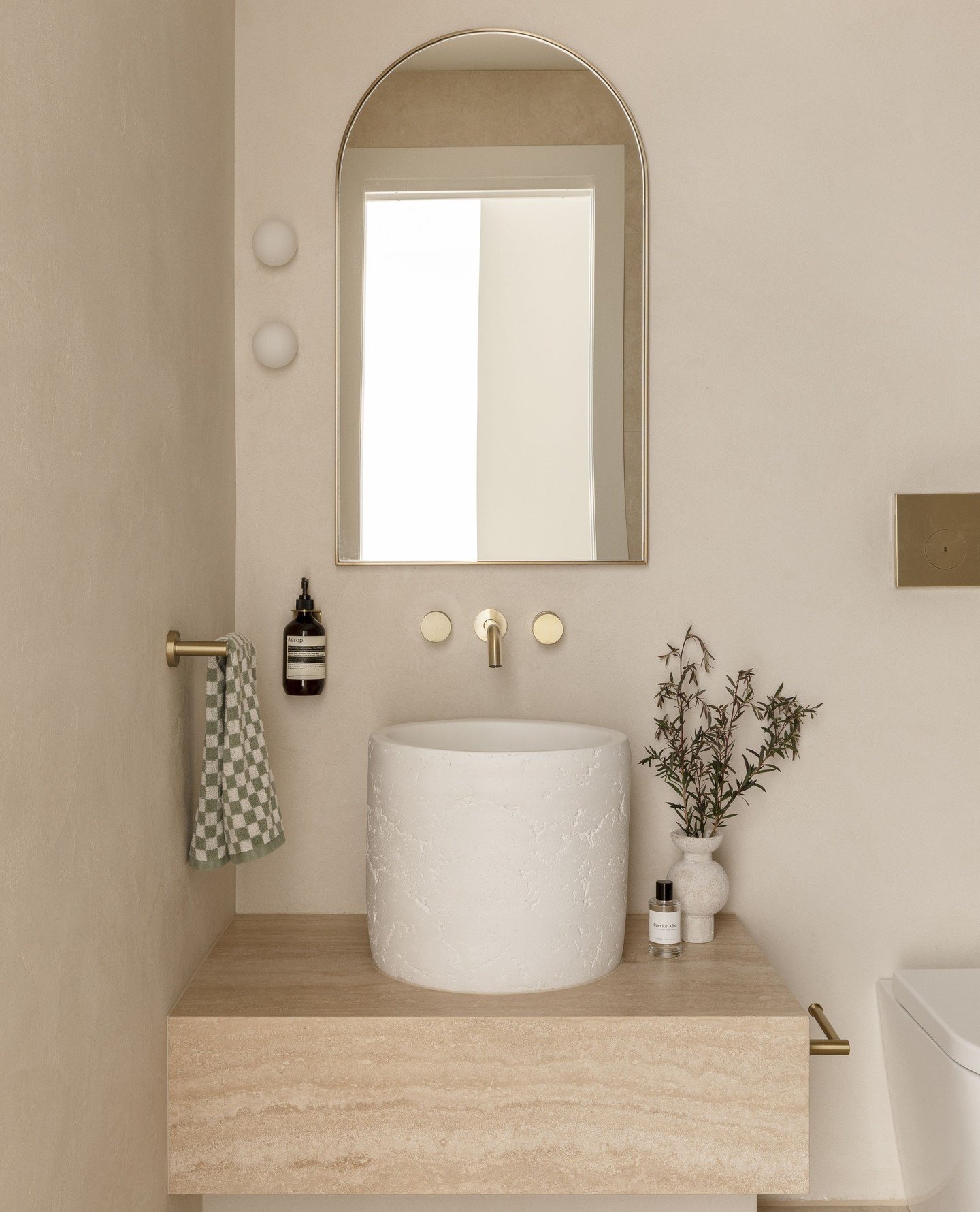 A simple brass hand towel bar mounted to the left of a round sink, holding a checkered green and white hand towel.