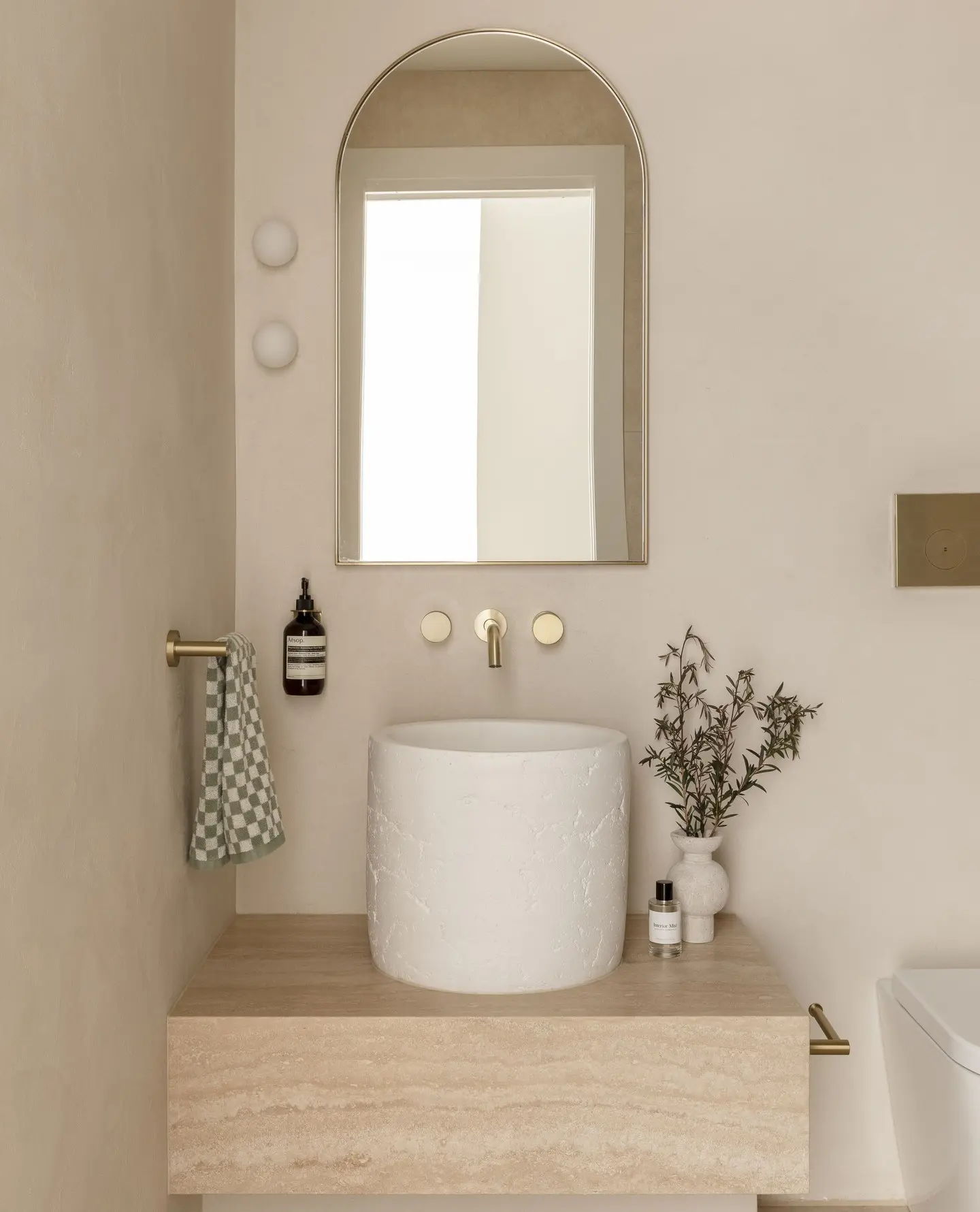 A simple brass hand towel bar mounted to the left of a round sink, holding a checkered green and white hand towel.