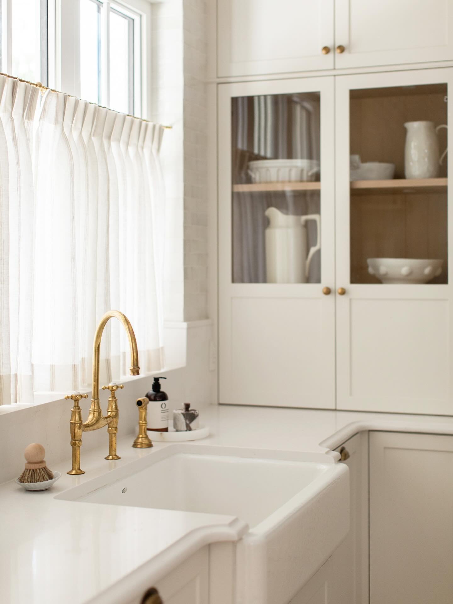 A bright white single-bowl undermount sink installed in a light countertop, paired with a traditional bridge-style faucet in polished brass.