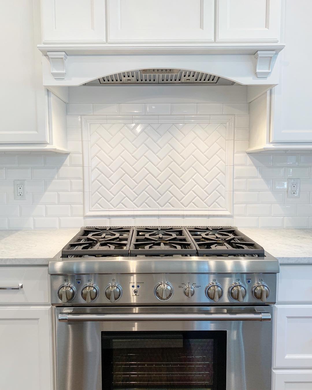Traditional white kitchen with a white subway tile backsplash and a framed inset panel of white dimensional herringbone tile above a stainless steel professional range.