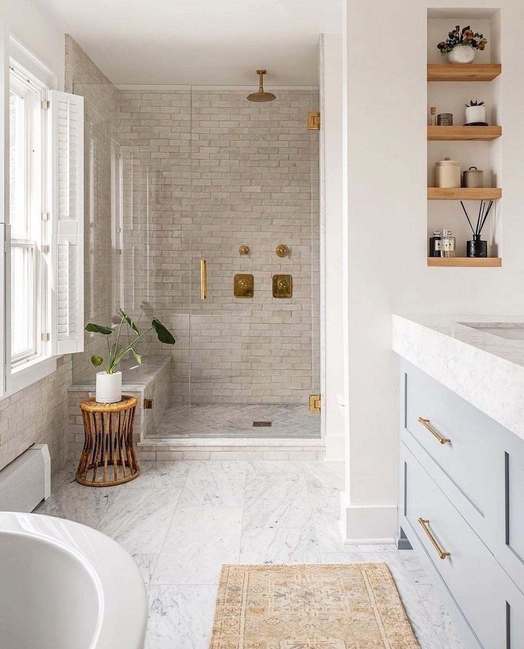 A bright bathroom with a shower tiled in light gray subway tiles, a pale blue vanity, and a floor of large square white and gray honed marble tiles.