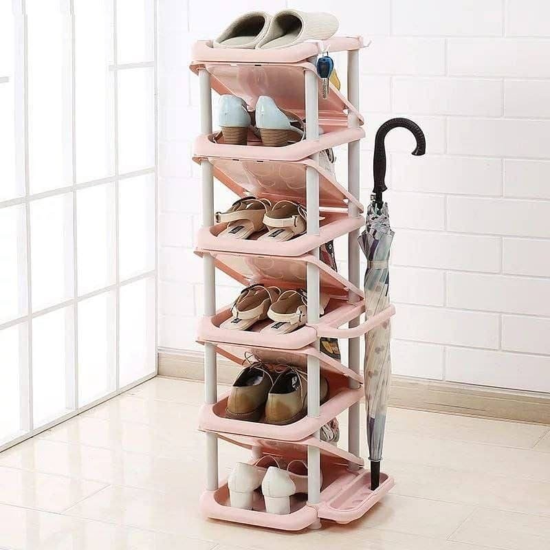 Six-tier pink plastic shoe rack with slanted shelves, storing various shoes and an umbrella hooked on the side.